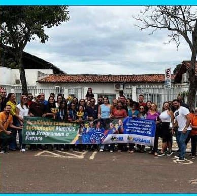 Grupo grande com faixa de projeto de tecnologia em frente a uma escola